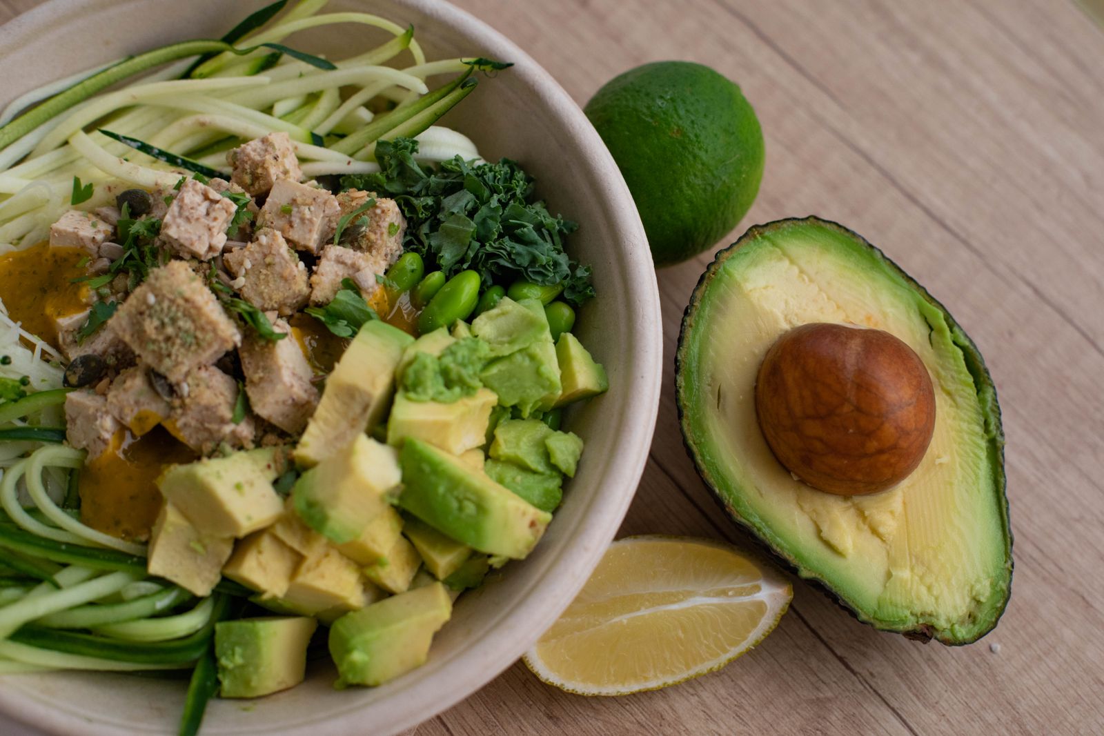 Vegansk skål med zucchininudlar, tofu, avokado och edamame, garnerad med lime