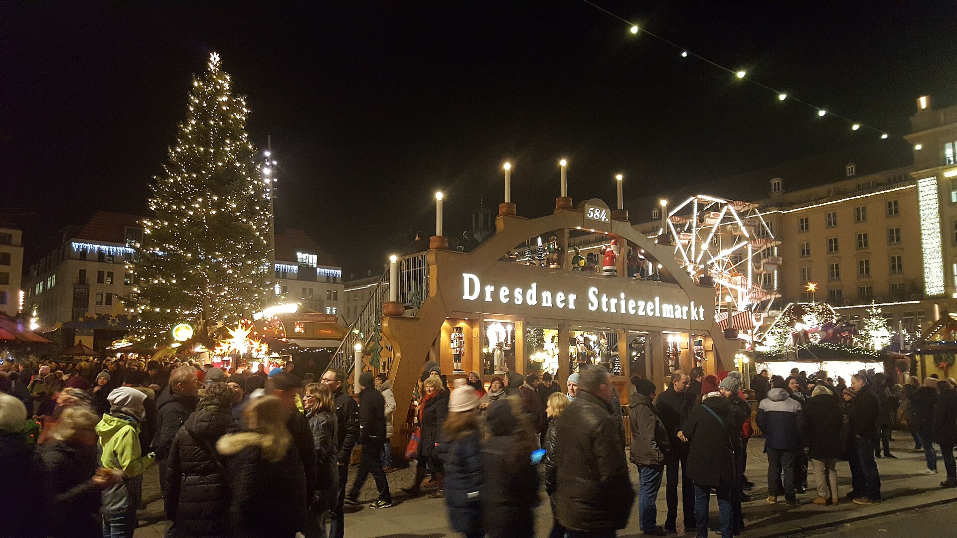 Den gångbara ljusbågen med texten Dresdner Striezelmarkt på Altmarkt i Dresden, med julgran och pariserhjul bakom