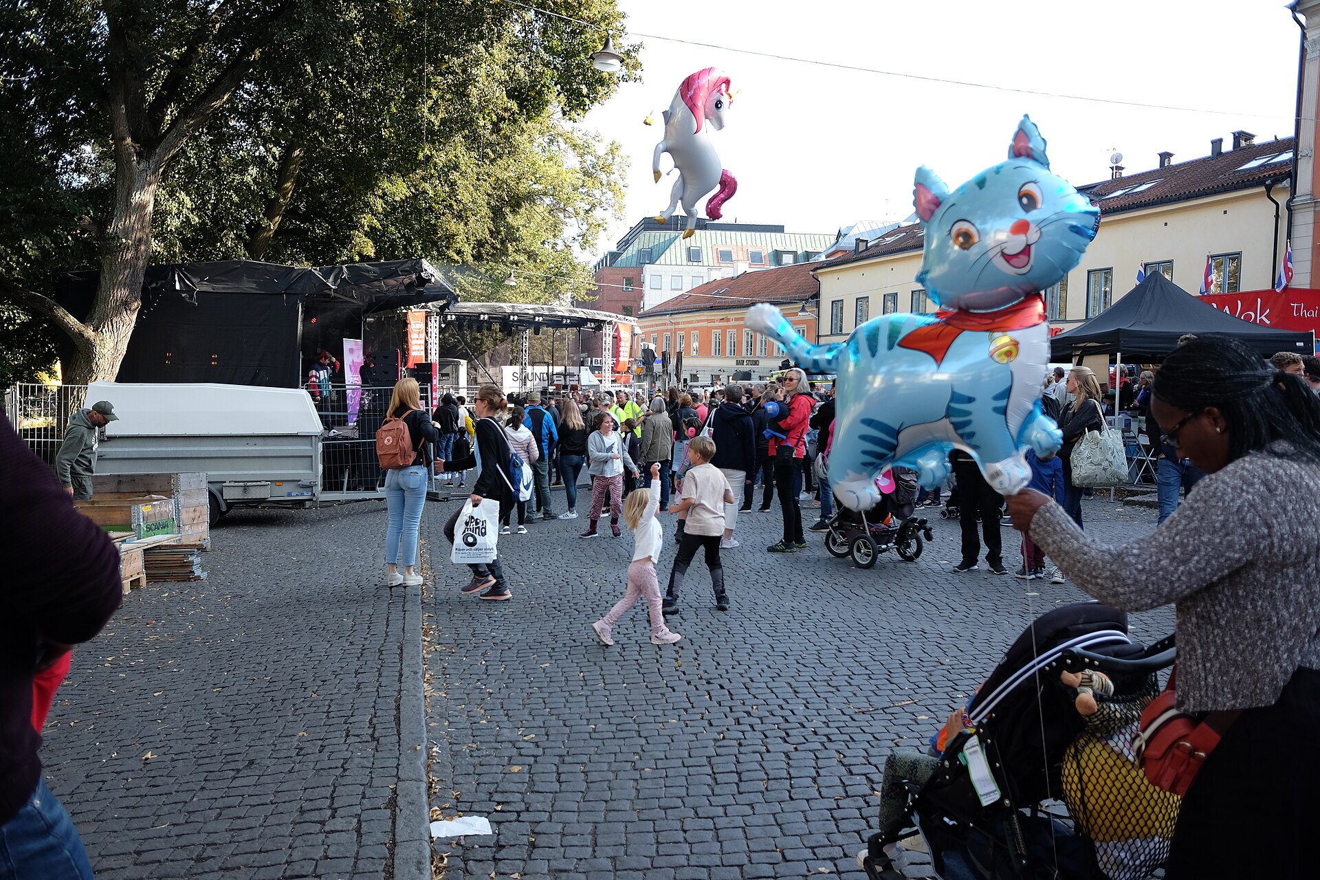 Folkliv och barnfamiljer på ett torg i Uppsala under Kulturnatten 2019, med en scen och ballonger formade som en katt och en enhörning