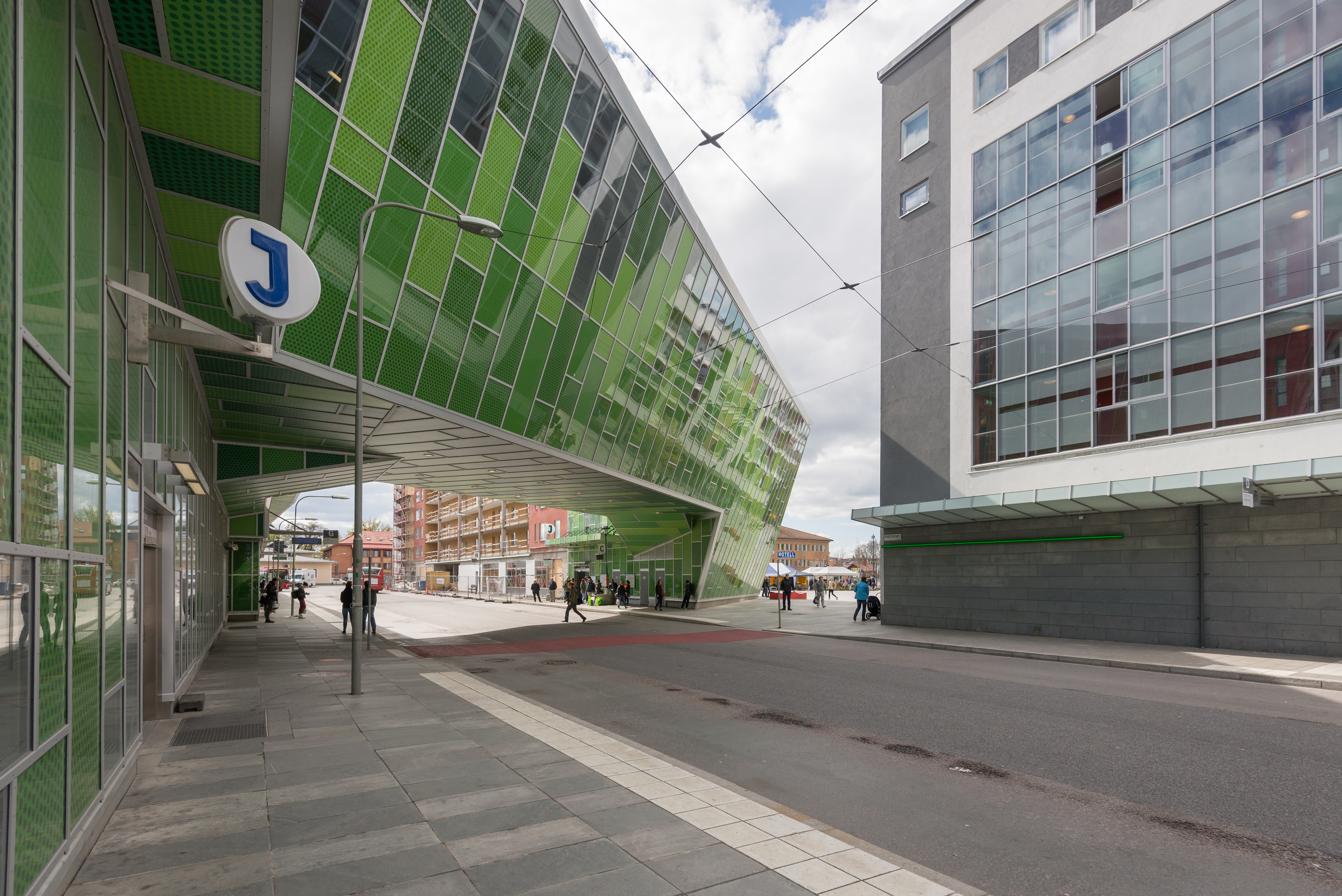 Älvsjö stations gröna stationsbyggnad med pendeltågsskylt och gående resenärer