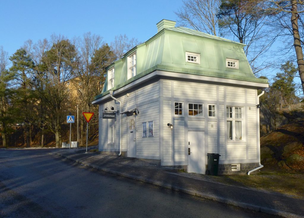 Den vita grindstugan med grönt mansardtak vid infarten till Långbroparken.