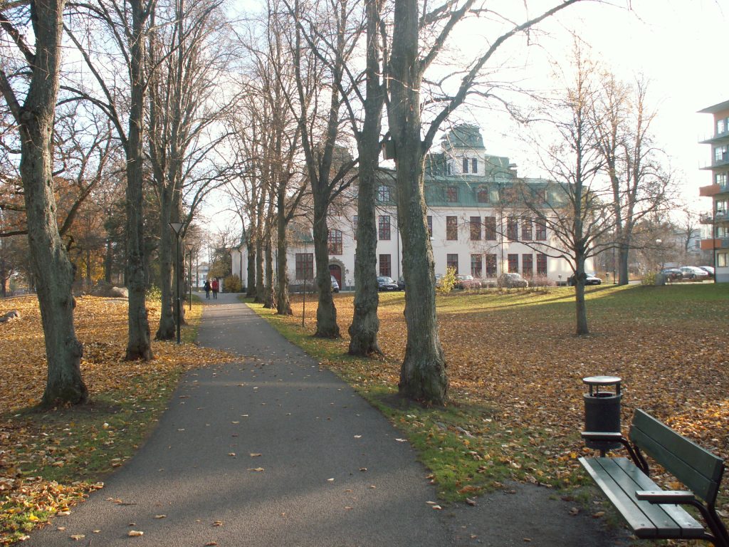 Stora Kvinns i Långbroparken, ett stort ljusputsat hus med grönt mansardtak och tornhuv.