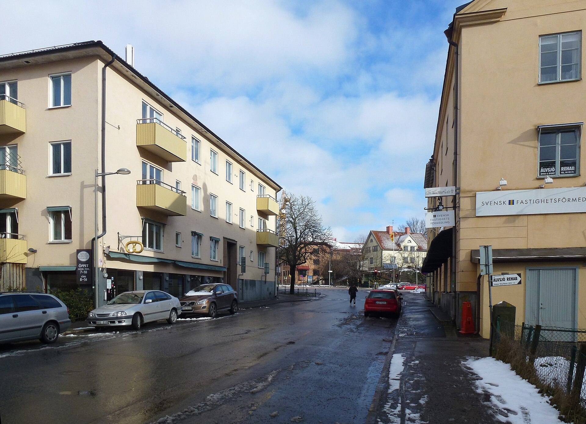 Johan Skyttes väg i Älvsjö en vinterdag, med bostadshus, butiker i bottenvåningen och en kringla som bageriskylt