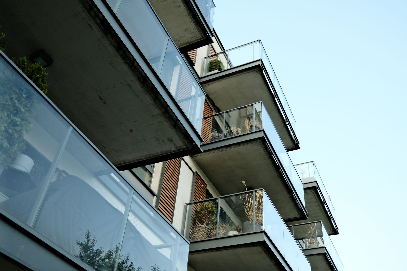 Modernt bostadshus med vita betongbalkonger och glasräcken mot klar himmel