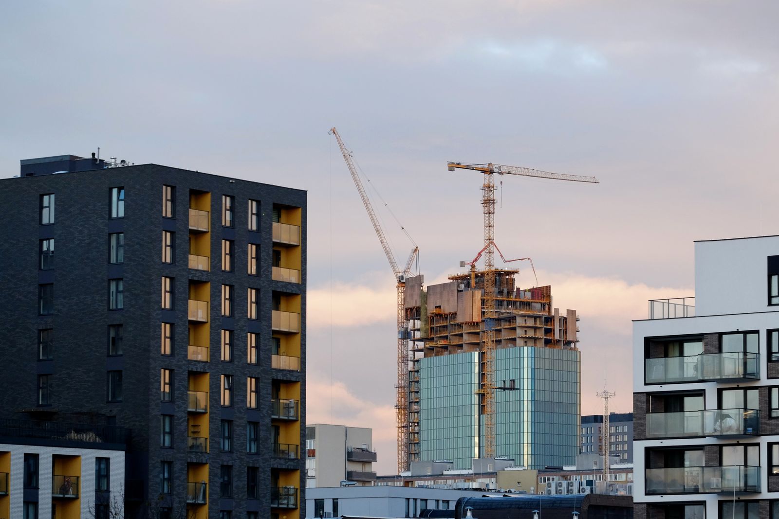 Nybyggda flerbostadshus och byggkranar i ett växande bostadsområde i skymning