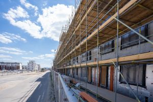 Byggnadsställning på ett nybyggt flerbostadshus med nytt bostadsområde i bakgrunden