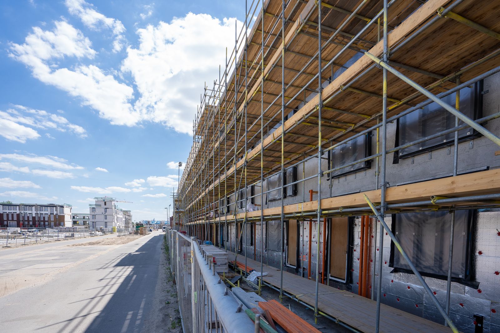 Byggnadsställning på ett nybyggt flerbostadshus med nytt bostadsområde i bakgrunden
