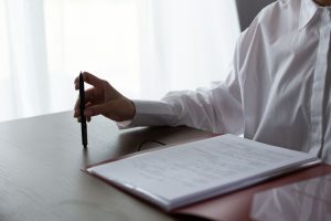 Person vid ett bord med penna och en uppslagen pärm med ifyllda blanketter