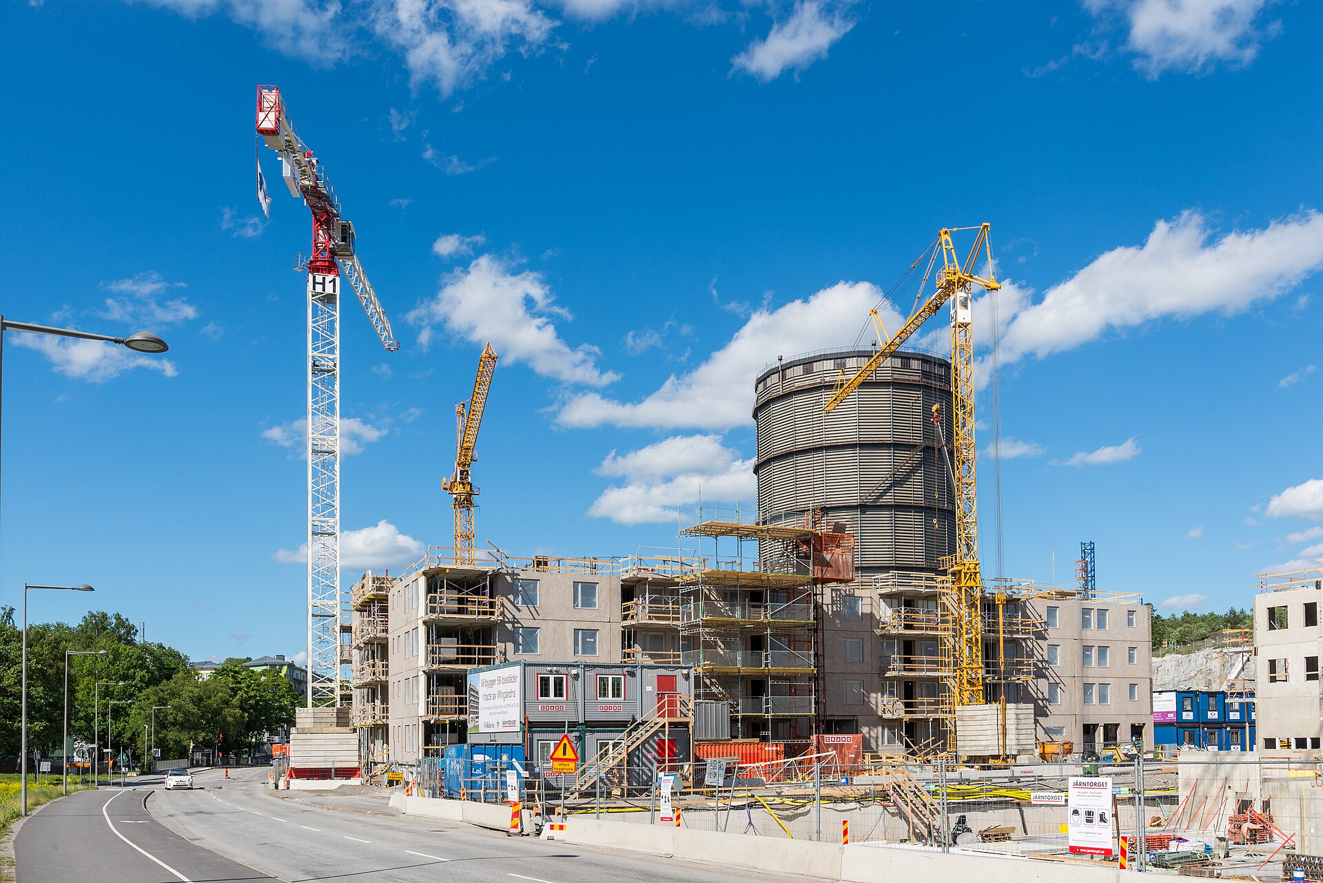 Flerbostadshus under uppförande med byggkranar och en gasklocka i bakgrunden