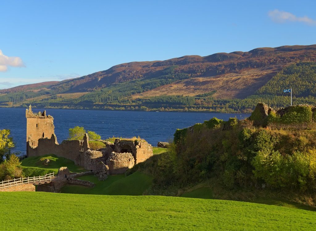 Urquhart Castles ruiner på klippudden vid Loch Ness i kvällssol, med sjön och Great Glens sidor bakom