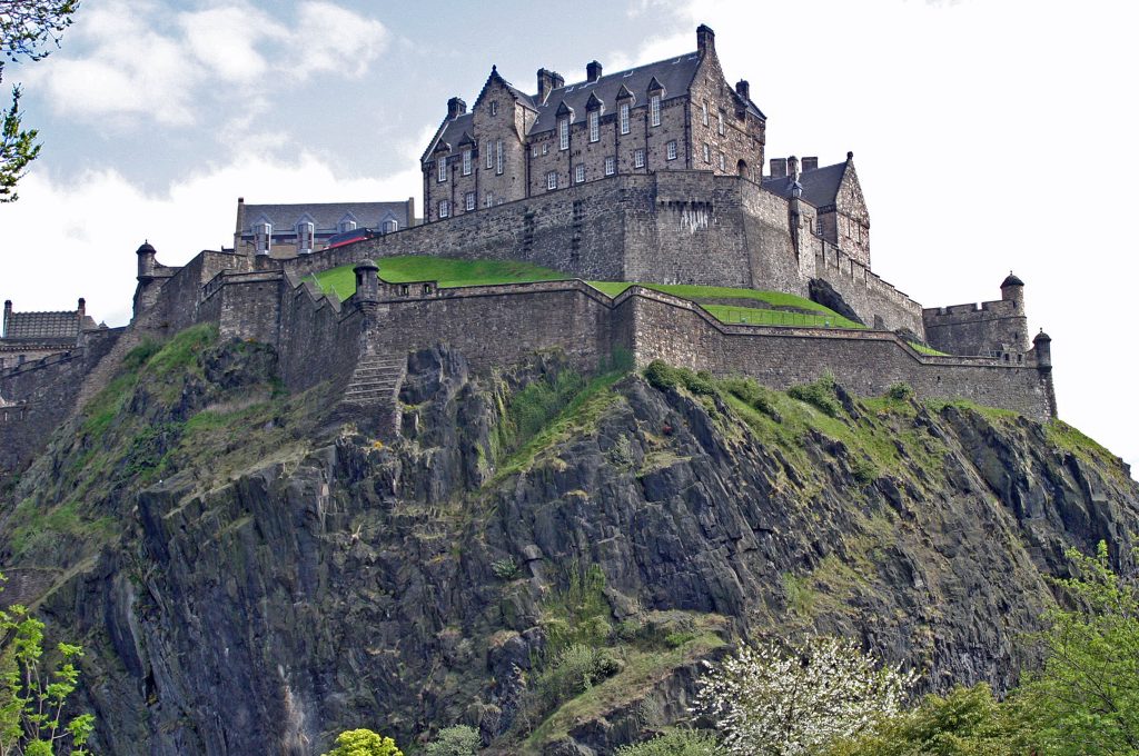 Edinburgh Castle högst upp på Castle Rock, med den branta klippsidan och grönska nedanför murarna