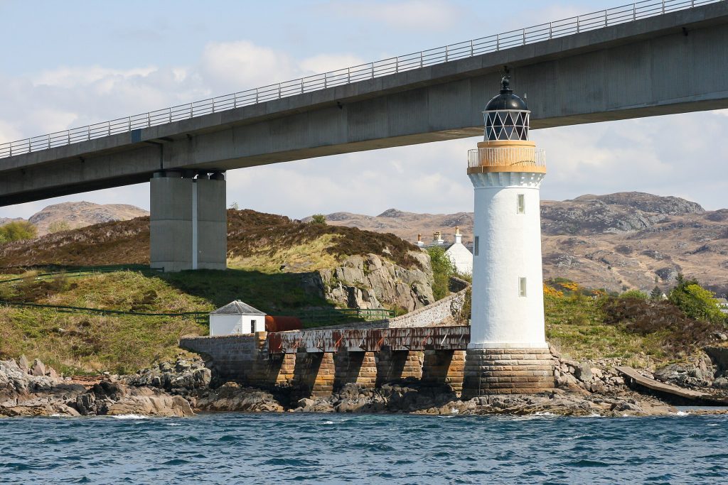Skye Bridges raka betongdäck vilar på en kraftig rektangulär pelare vid Kyleakin, med den vitmålade fyren på Eilean Bàn i förgrunden