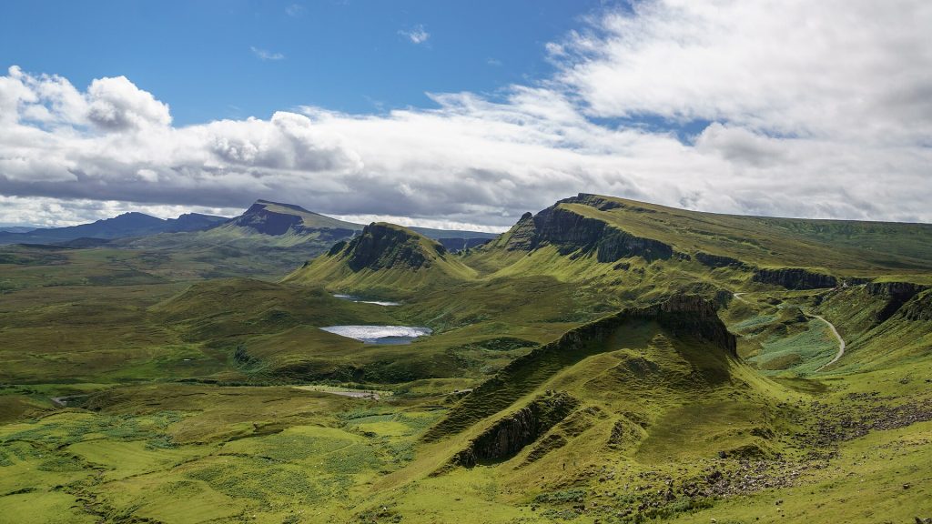 Quiraings gröna klippterrasser och rasbranter på norra Skye, med den smala vägen synlig längs bergssidan