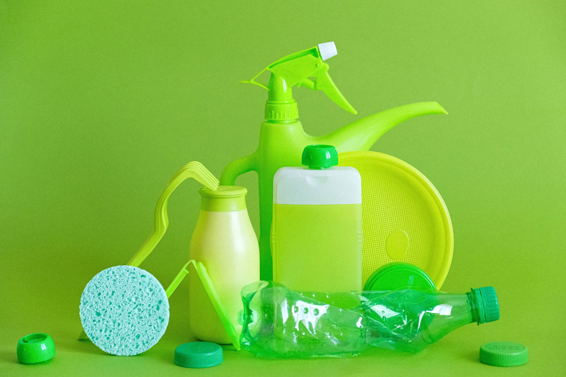 Gröna plastflaskor, en sprayflaska och en tillplattad PET-flaska mot en grön bakgrund