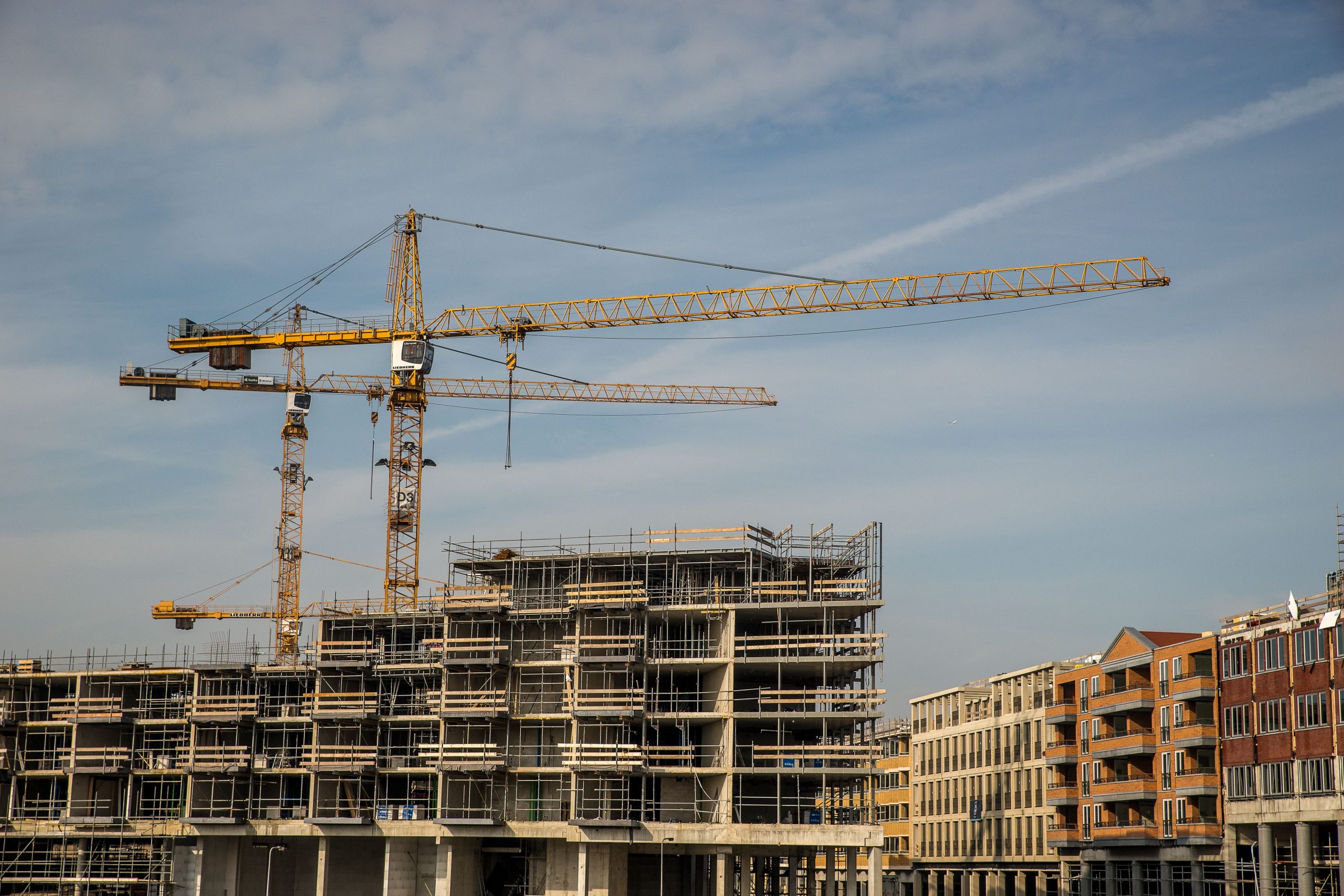 Flerbostadshus under uppförande med två byggkranar, intill färdiga bostadshus