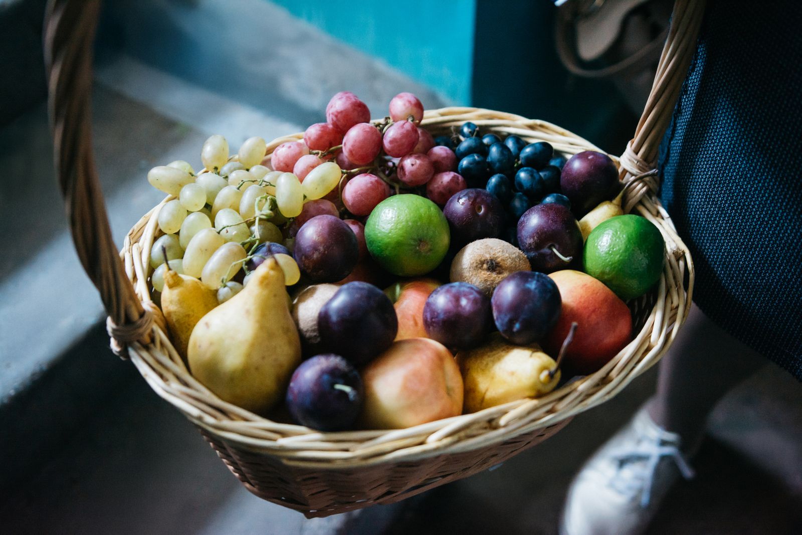 Person bär en flätad korg full med frukt