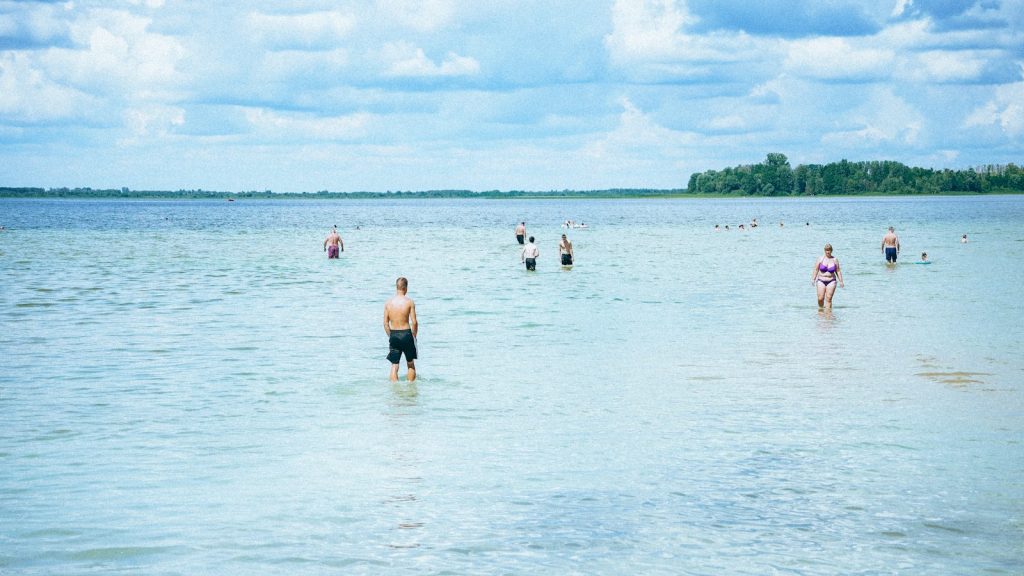 Badande som vadar ut i en grund, klar sjö en solig sommardag.