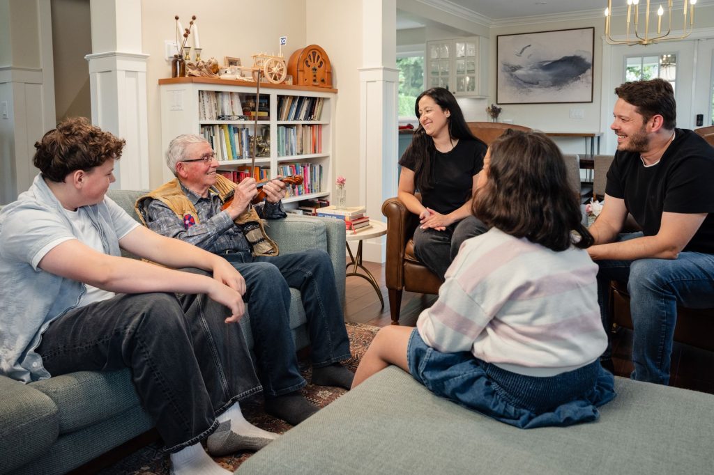 Tre generationer i en familj samlade i ett vardagsrum och samtalar med varandra