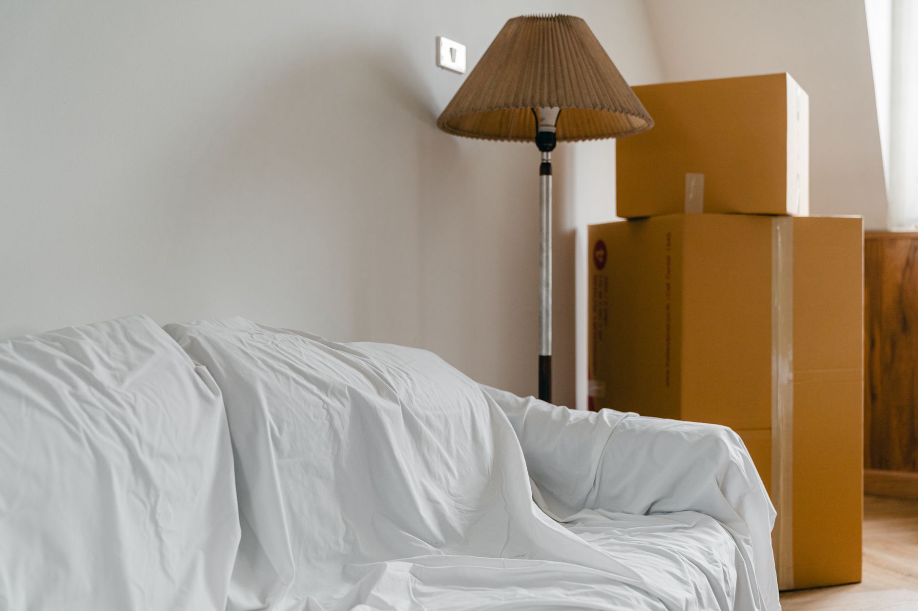 Flyttkartonger, golvlampa och en soffa täckt med lakan inför en flytt