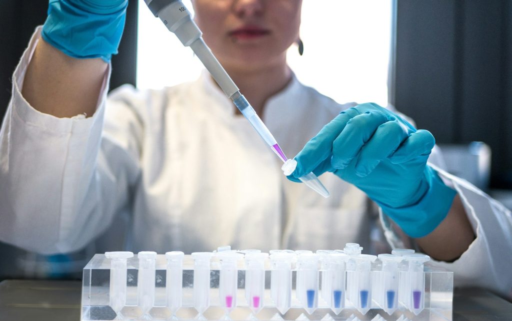 Forskare i labbrock pipetterar färgade prover till provrör i ett forskningslaboratorium