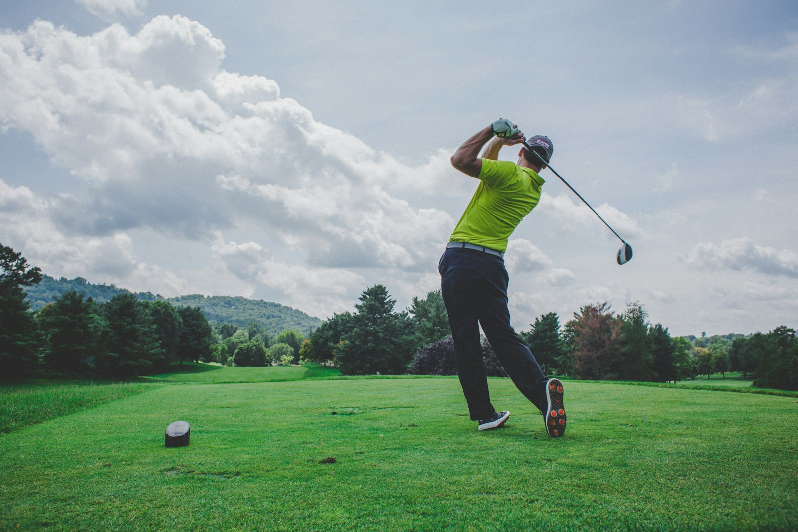 Golfare i utsving med driver på en grön, trädkantad golfbana