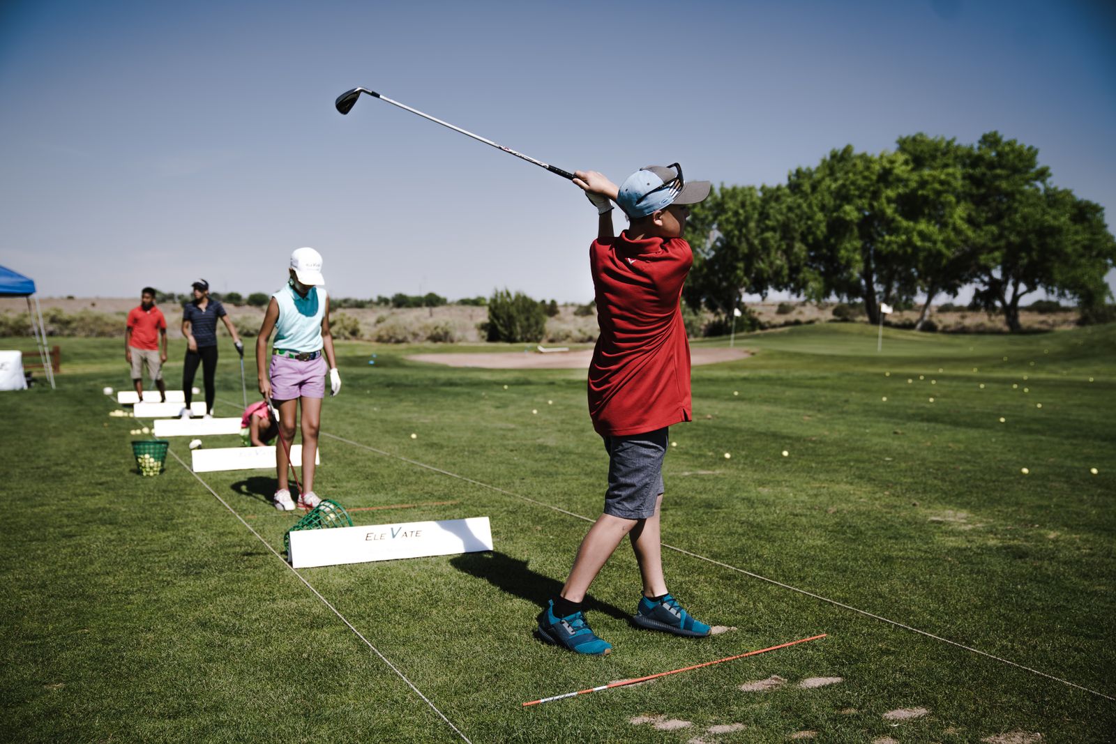 Nybörjare som övar golfsving på en driving range en solig dag