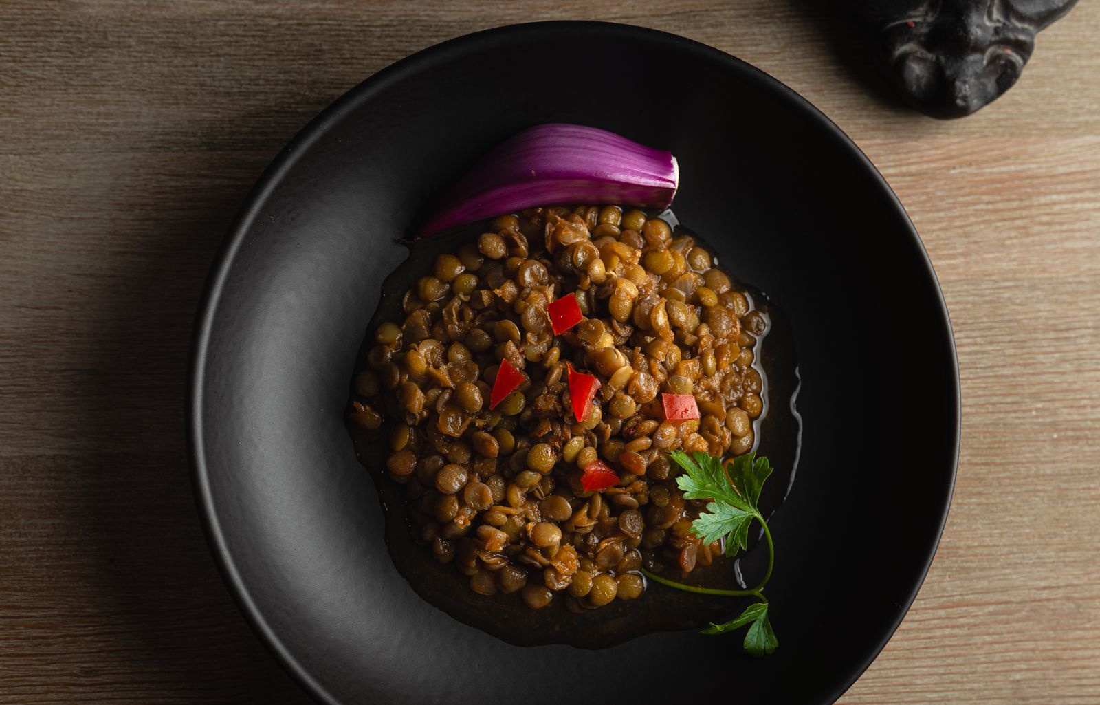 Kokta gröna linser i svart skål med rödlök, chili och persilja