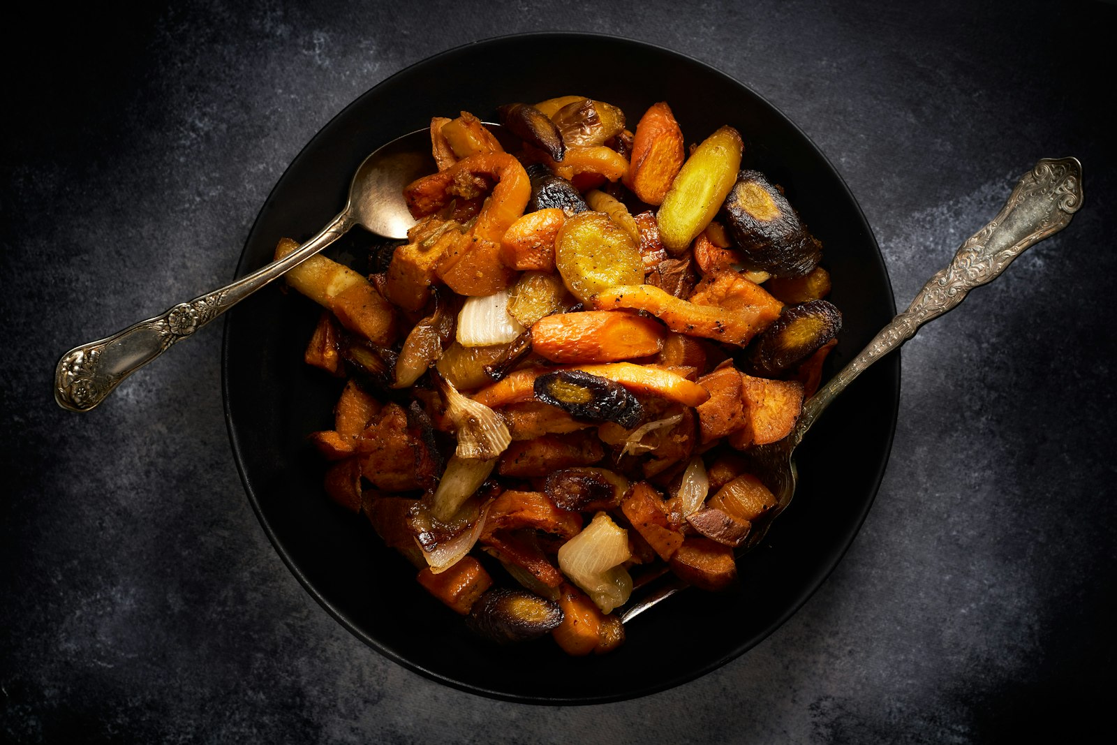 Rostade rotfrukter med morot, sötpotatis och lök i en svart skål