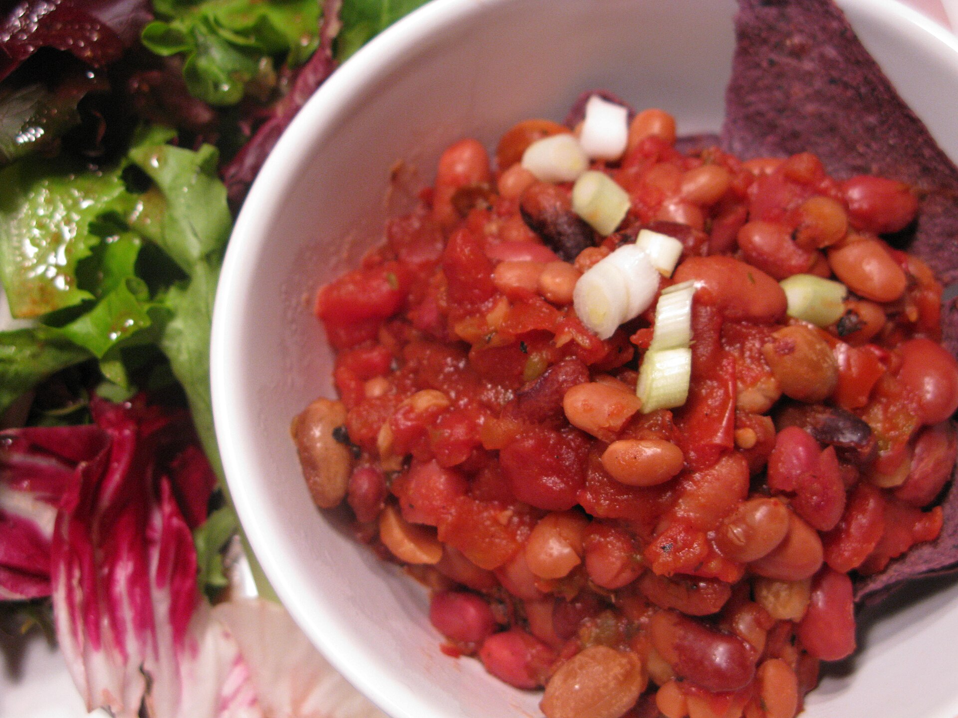 Vegansk bönchili med salladslök i en vit skål