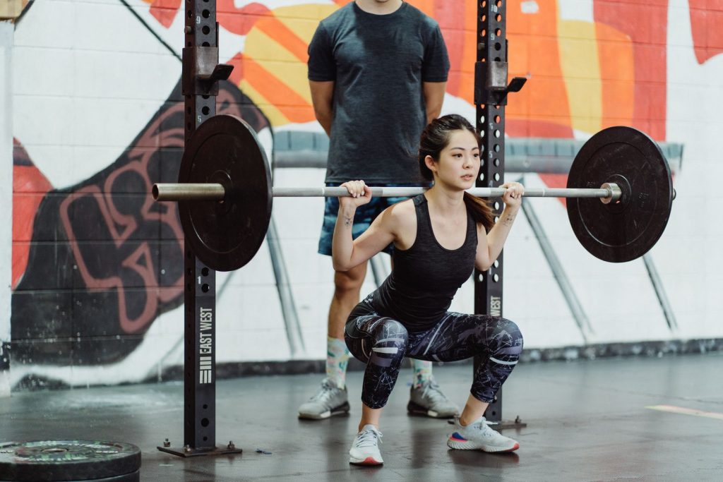Kvinna i löparskor gör en skivstångsknäböj i ett gym