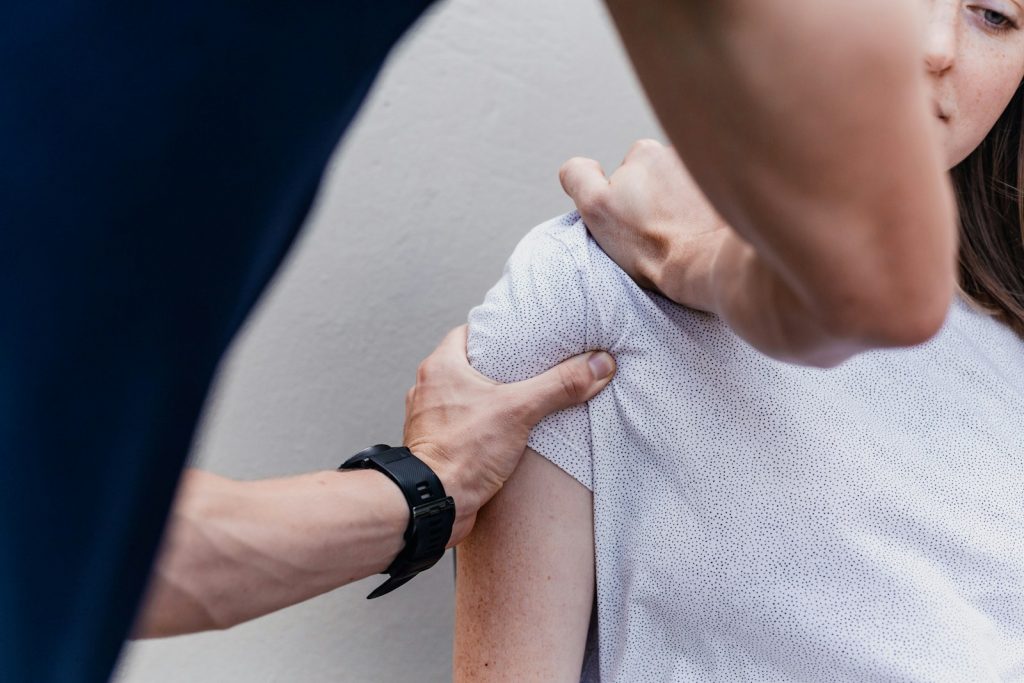 En behandlare håller med båda händerna om axeln på en kvinna som vrider på nacken