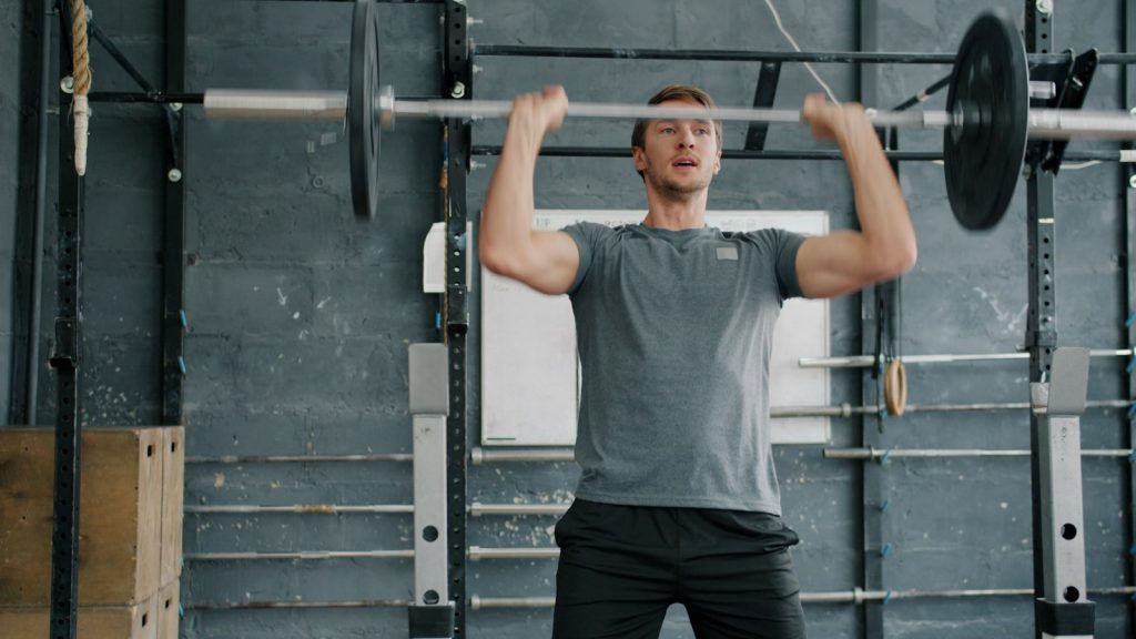 Man gör stående axelpress med skivstång i ett gym