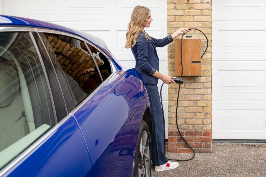 Kvinna tar laddkabeln från en väggmonterad laddbox vid garaget