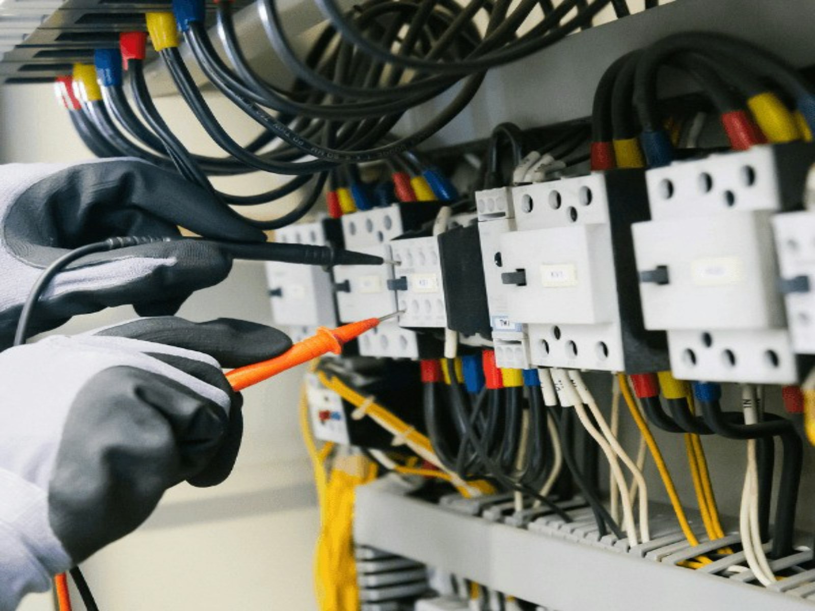 Elektriker med skyddshandskar mäter spänning med multimeter i en elcentral med dvärgbrytare och färgmärkta ledningar