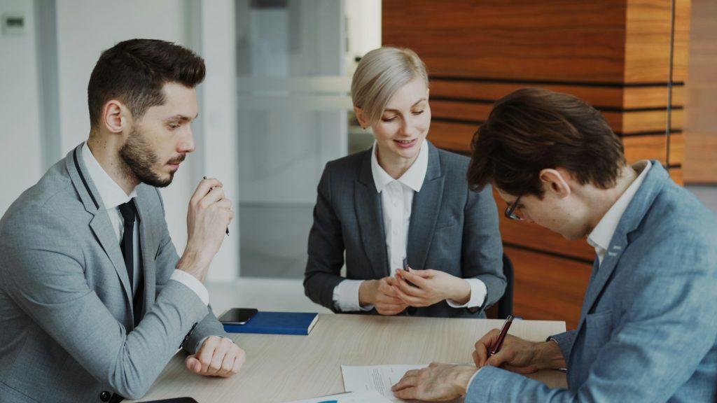 Three people in business attire reviewing and signing a document in an office