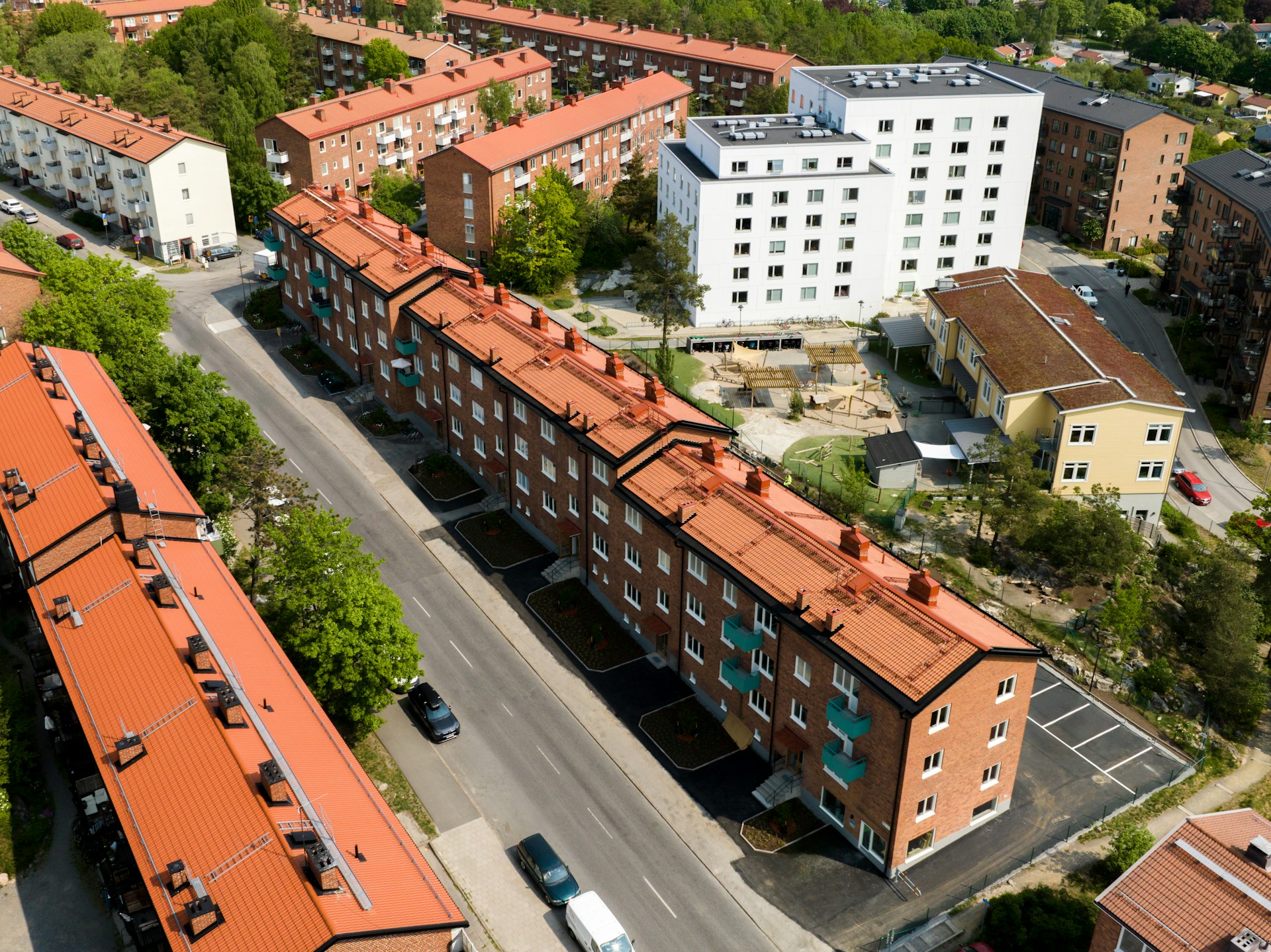 Flygbild över ett bostadsområde med rader av äldre flerbostadshus i tegel och ett nyare vitt hus intill