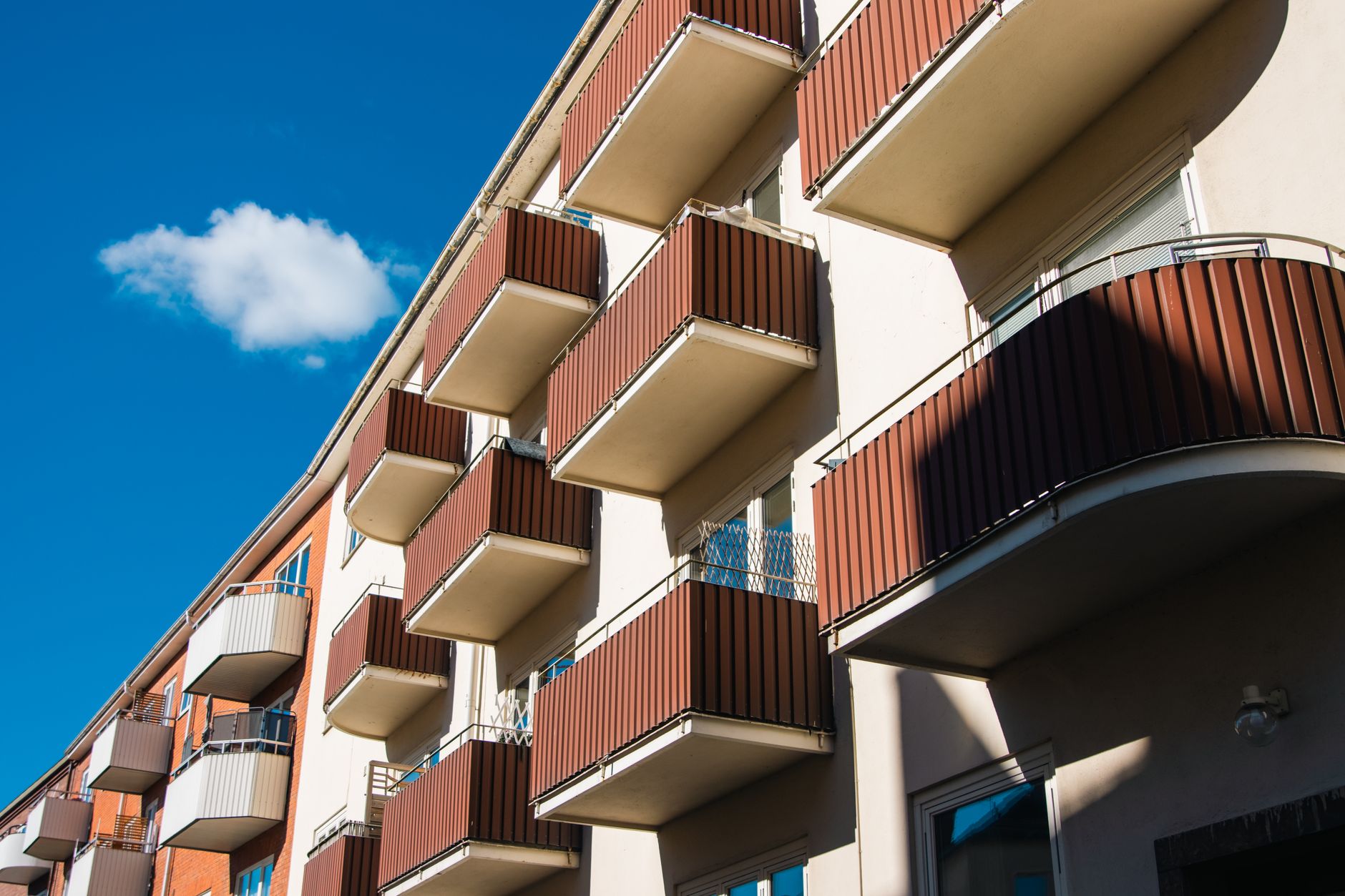 Flerbostadshus med rödbruna balkonger mot blå himmel