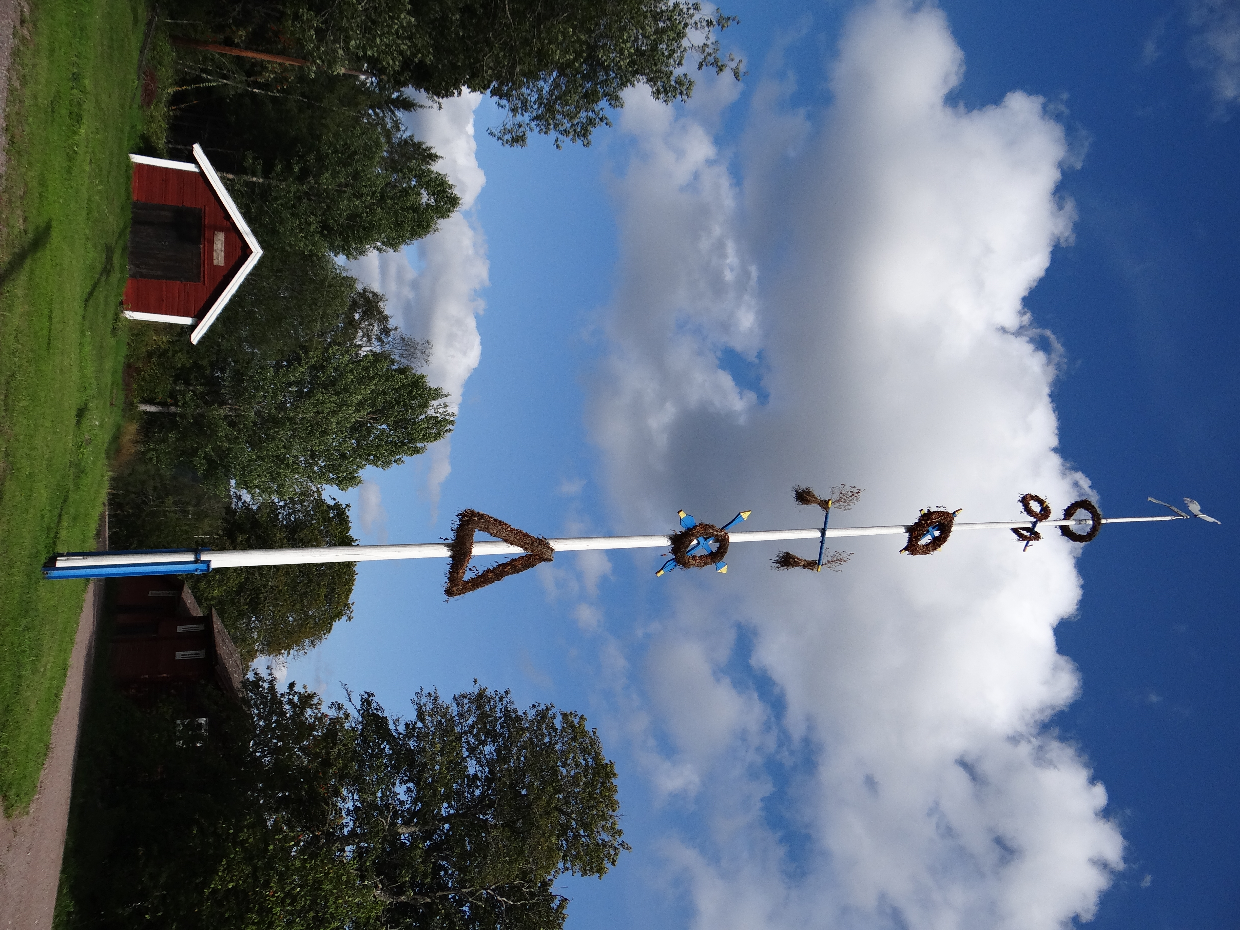 Majstång klädd med lövade ringar och kransar mot blå sommarhimmel i Leksand