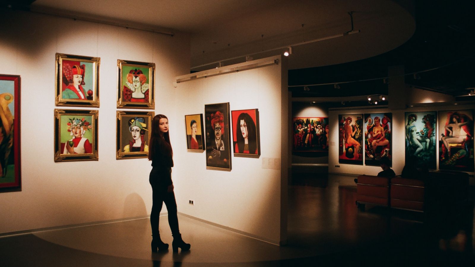 Besökare som betraktar färgstarka porträttmålningar på en vägg i ett konstmuseum