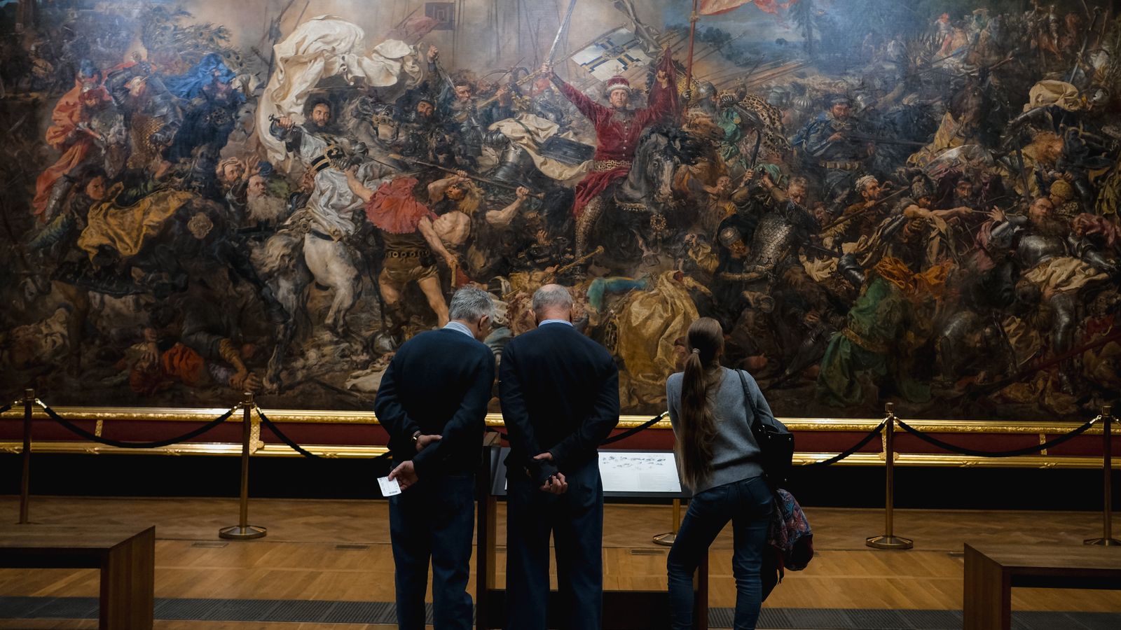 Museibesökare som studerar en stor historisk målning på nära håll