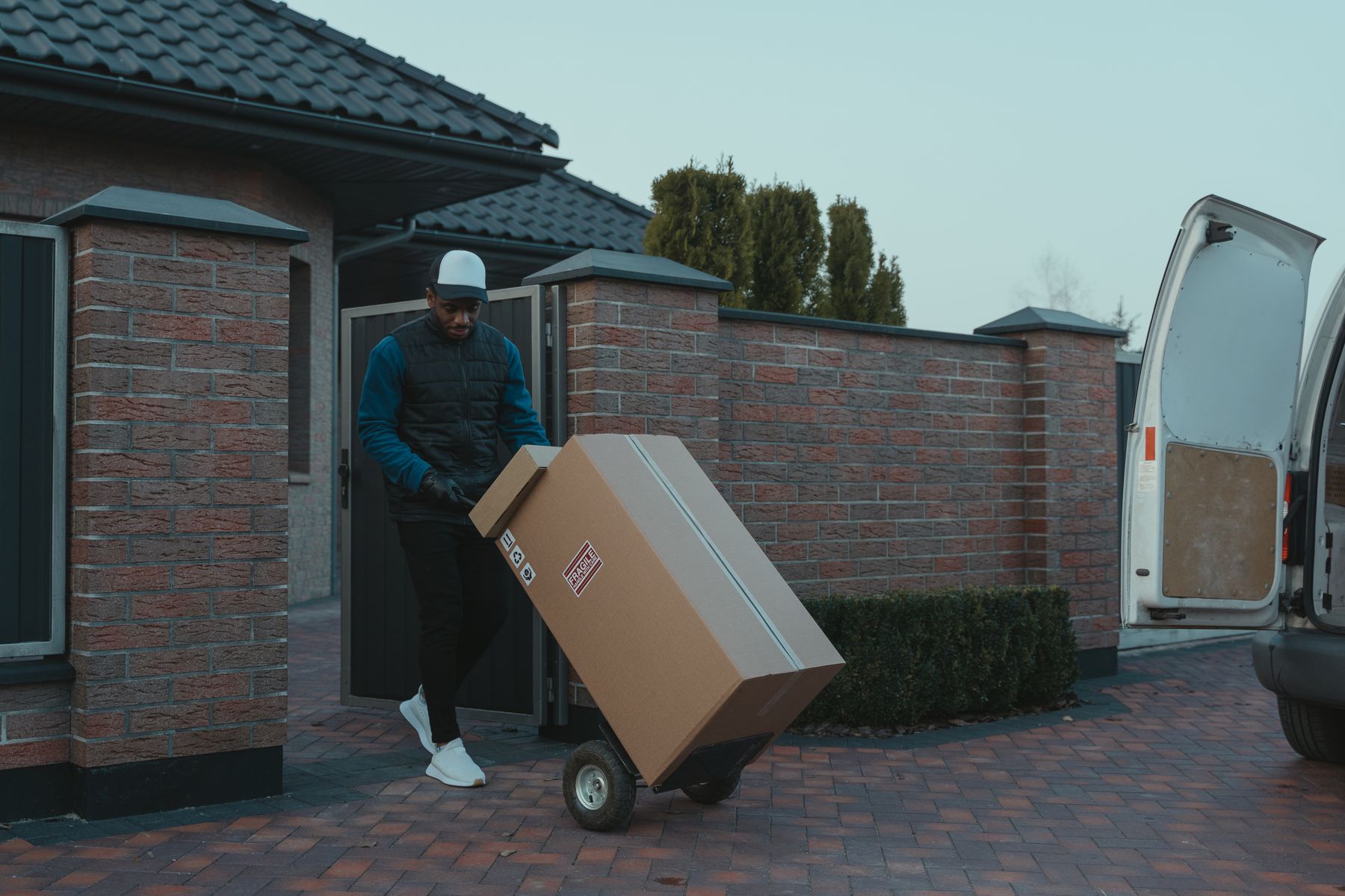 En flyttarbetare kör en säck med flyttlådor mot en flyttbil vid ett bostadshus