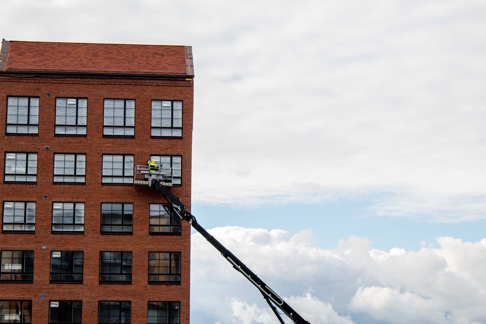Servicetekniker i skylift arbetar med fasaden pa ett rott tegelflerbostadshus