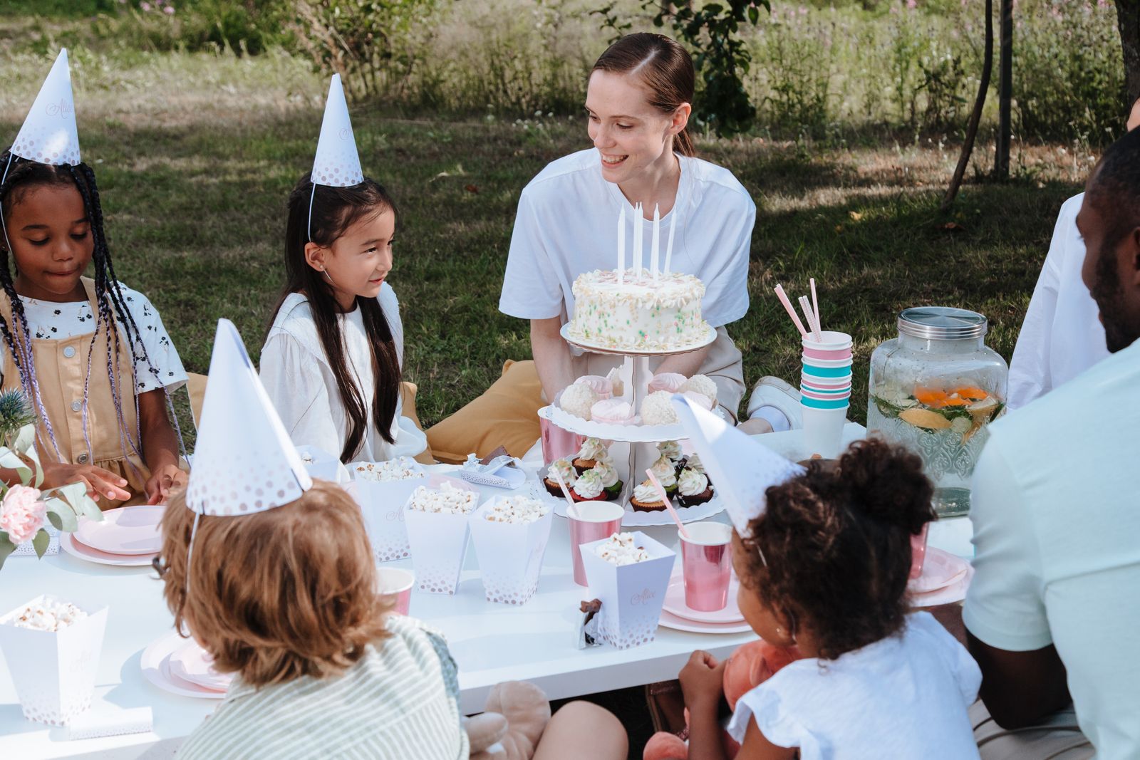 Barnkalas utomhus med tårta, cupcakes och barn i partyhattar
