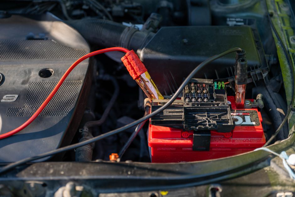Ett bilbatteri med startkablar i motorrummet