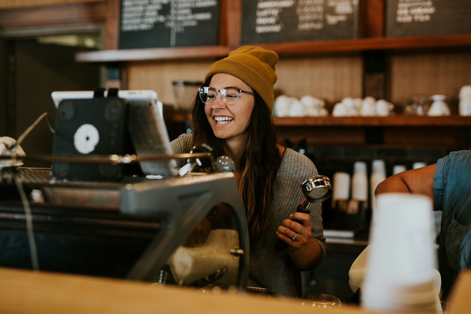 Ung kvinna som arbetar vid espressomaskinen på ett kafé
