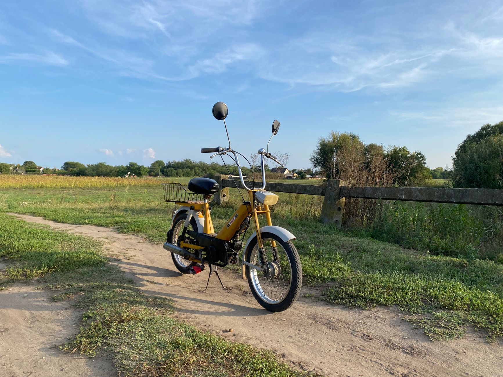 Gul äldre moped parkerad på en grusstig vid en hage