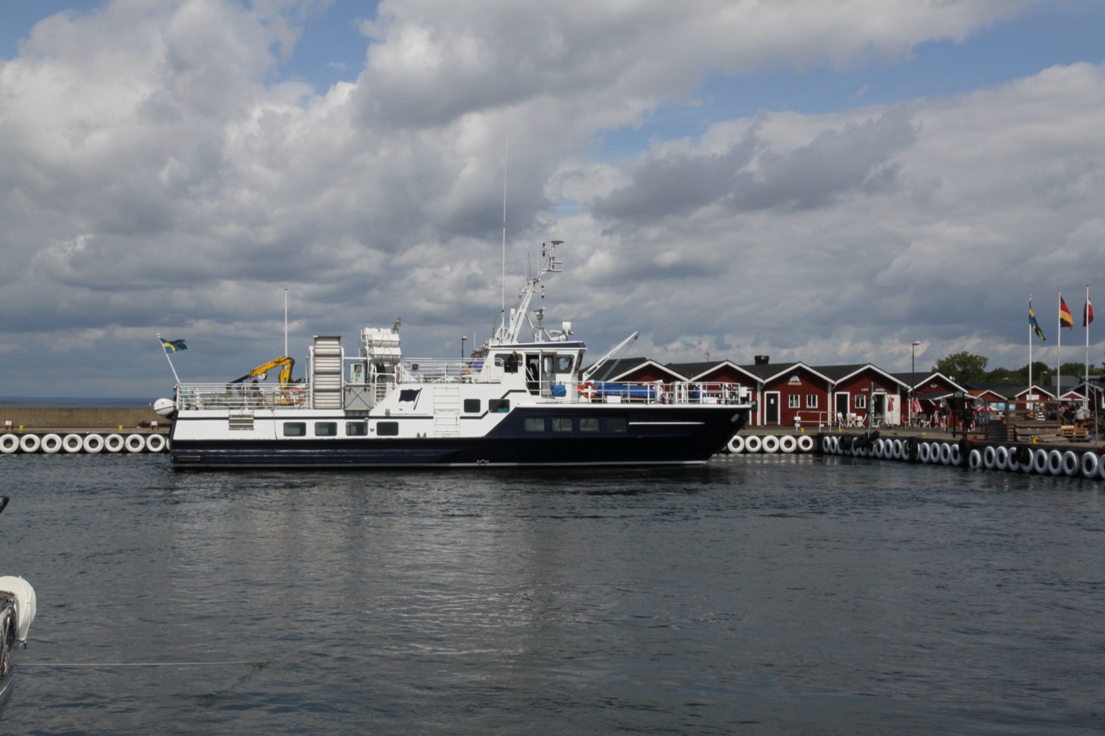 Färjan M/F Vitaskär vid kaj i Hanö hamn med röda sjöbodar bakom