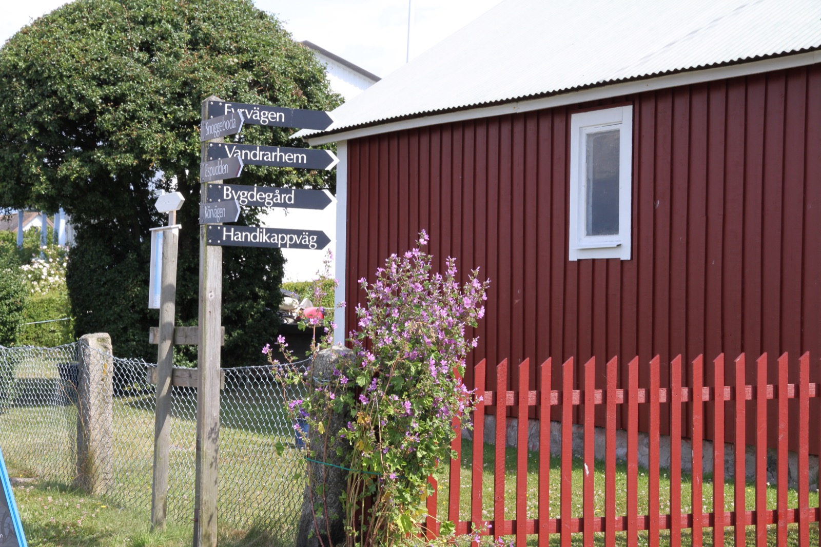 Vägvisare mot vandrarhem och bygdegård vid en röd stuga på Hanö