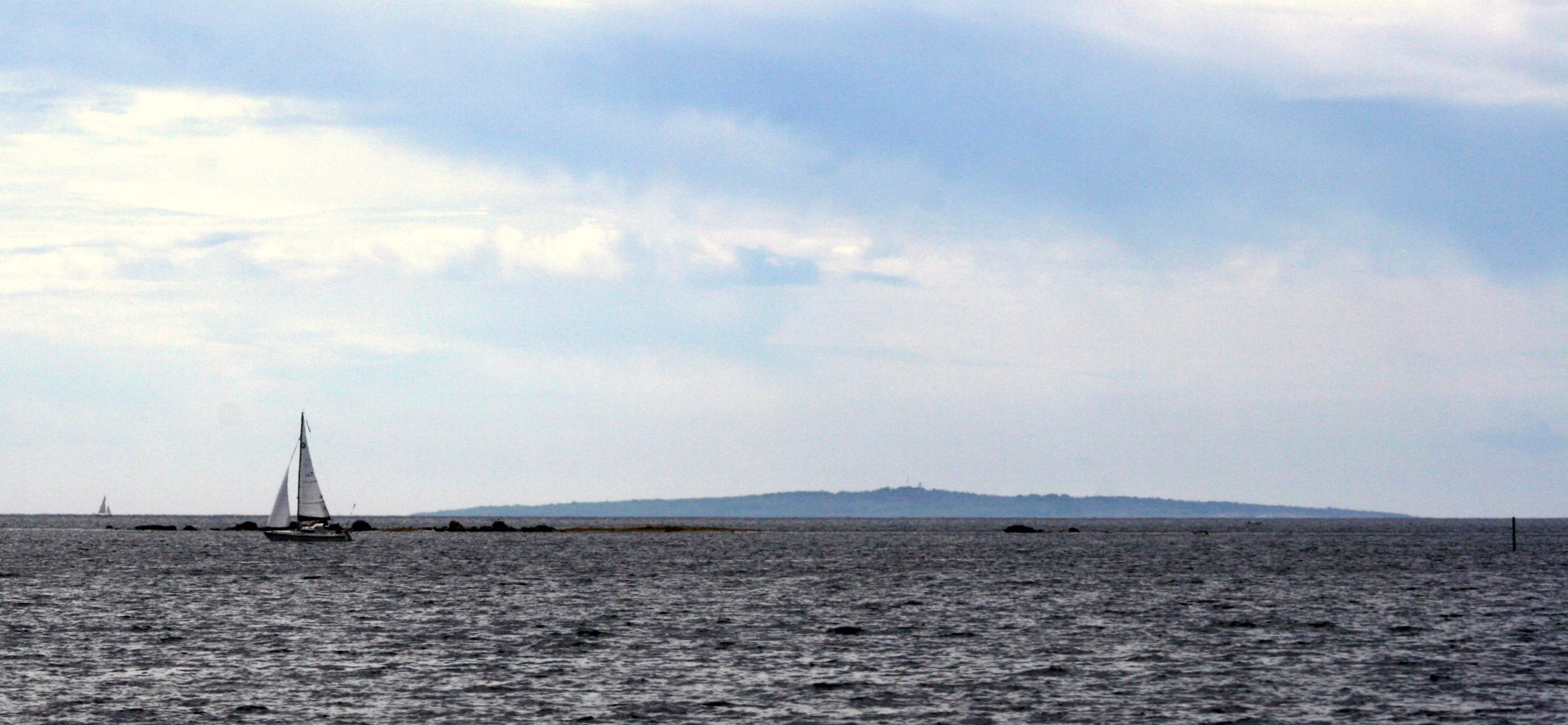 Hanö som en låg rygg vid horisonten sett över öppet vatten från Blekinges kust, med en segelbåt i förgrunden