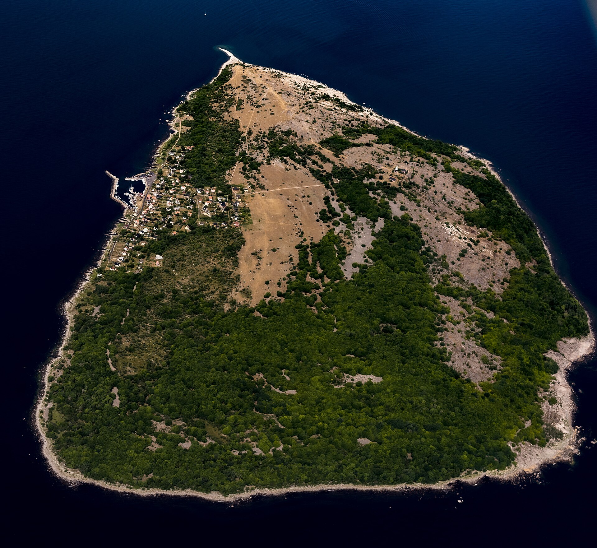 Flygfoto över Hanö med skog i söder, öppen mark i norr och byn vid hamnen